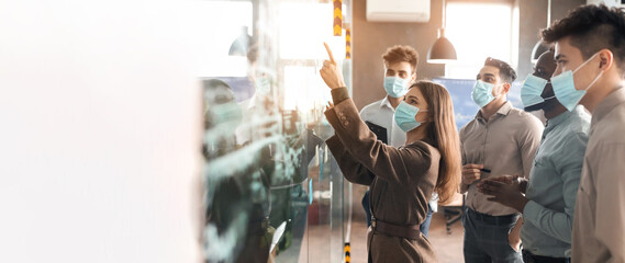 Busy serious international young people engineers businessmen in protective masks look at presentation