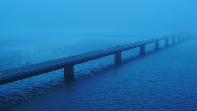 Aerial of traffic over the bridge Storebæltsbroen in Denmark. There is a heavy fog, and it is during the blue hour. 4K