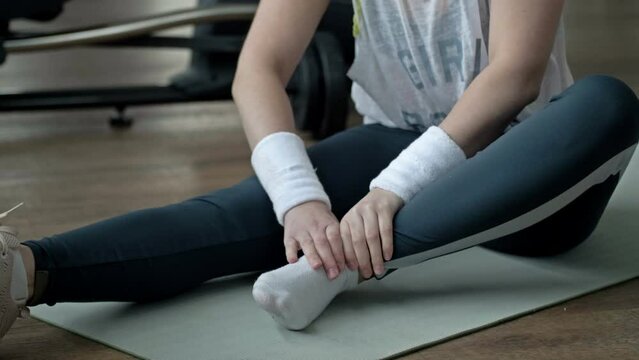 Young woman feels pain from an ankle injury while exercising at the gym.