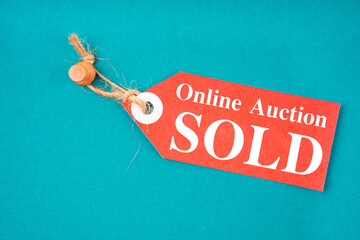 The red tag Online auction sold hanging with wooden push pin on green background.