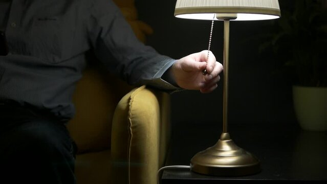 A man sits next to a table lamp and turns it off