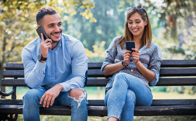 Social alienation. Young couple chatting and talking on a mobile phone while sitting on the park...