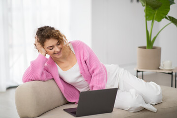 Happy Young Woman Relaxing With Laptop On Couch At Home