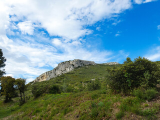 Fototapeta na wymiar Natural landscape of the Alpilles in Provence in France where a rocky outcrop rises from a hill covered in scrubland under a beautiful blue sky adorned with pretty light fluffy white clouds