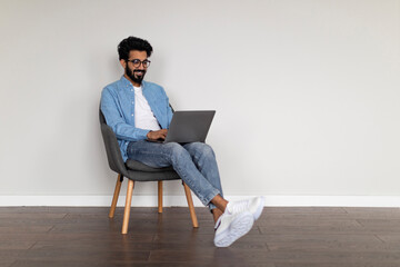 Young Indian Freelancer Guy Using Laptop While Sitting In Armchair At Home