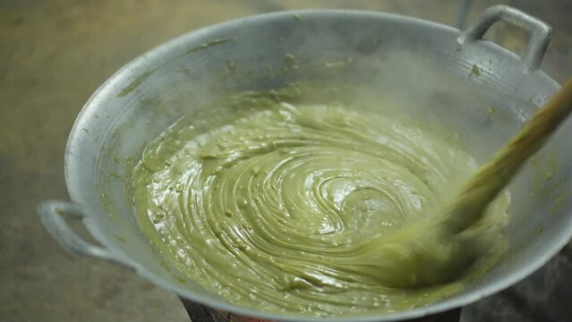 cooking liquid rhombic pandan leaf stirring or closeup fresh kanom piak poon bai toey and green coconut sweet pudding with smoke steam heat on hot pan to charcoal stove by thailand nature dessert food