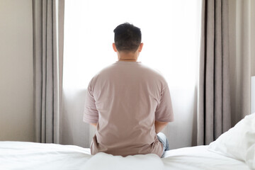 Unhappy man sitting alone on bed alone at home