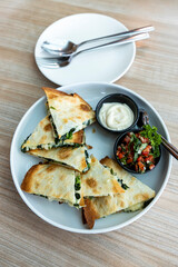 Quesadilla in a round plate, next to an empty plate and cutlery, on a wood grain table, natural light. Selective focus.