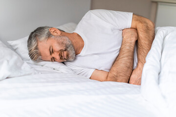 Fototapeta na wymiar Middle aged man lying in bed, suffering from stomach pain