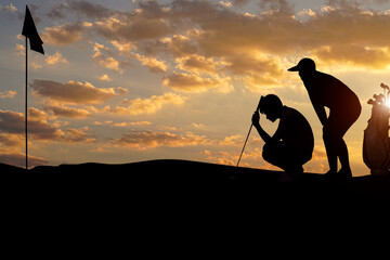 Golfers' hit golf ball toward the hole at sunset silhouetted