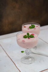 Two glasses with strawberries puding on white table in brown background.
