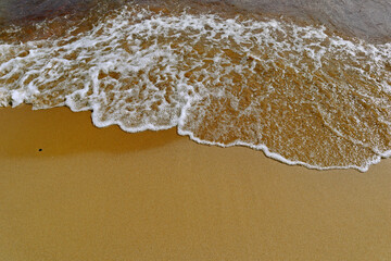 Soft wave with white foam close-up. Sandy seashore on a sunny summer day.