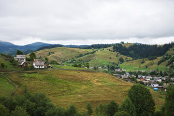 Obraz premium Traditional ukrainian houses in mountain village in summer. Mountain valley in Ukraine. Rural landscape with buildings, green grass, trees on the hill