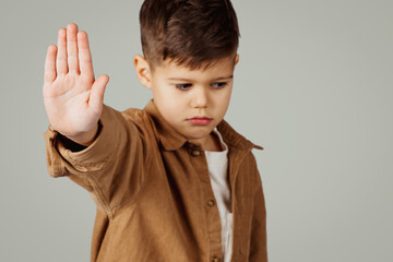 Sad caucasian 6 years old little boy show stop gesture with hand isolated on gray studio...