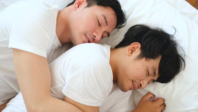 Asian LGBTQ gay couple in white t-shirts cuddling on the mattress and smiling with happy faces.