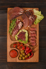 Dried Processed Beef Jerky with spices and vegetables on wooden board against dark background.Slicing.Flat lay. Vertical