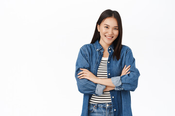 Sassy korean girl, stands in confident pose, smiles and looks self-assured and motivated, white studio background