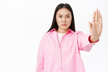 Stop. Serious korean woman shows prohibit, taboo sign, extends palm, rejects or forbids smth,...