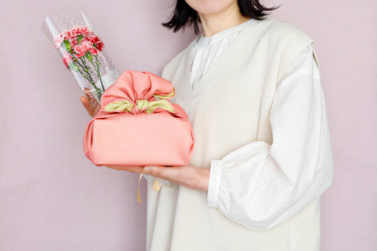 花束とプレゼントを持つ女性　ピンク背景　春のイメージ