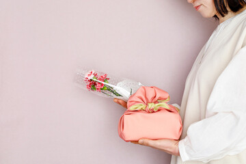 花束とプレゼントを持つ女性　ピンク背景　春のイメージ
