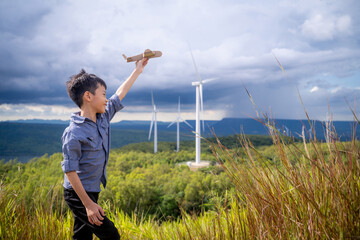 Happy Asian boy playing toy plane with wind turbine in the background. © Jirus