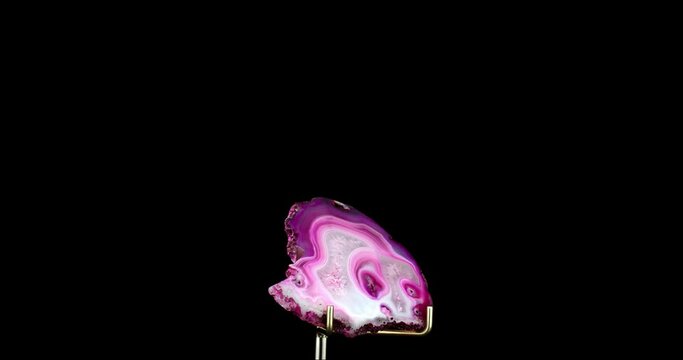 Pink tainted agate slice on support 360&deg; rotation in 4k. macro detail texture background. close-up raw rough unpolished semi-precious gemstone