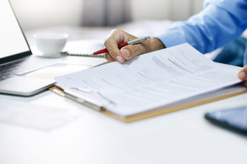 Asian businessman reviewing document reports at office workplace with computer laptop. legal expert, professional lawyer reading and checking financial documents or insurance contract