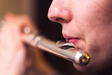 A portrait of the mouth of a flutist blowing into the mouth piece of a metal silver flute in order to play some notes of a musical piece.