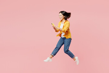 Full body young cheerful woman of Asian ethnicity wear yellow shirt white t-shirt jump high hold in hand use mobile cell phone run fast isolated on plain pastel light pink background studio portrait.