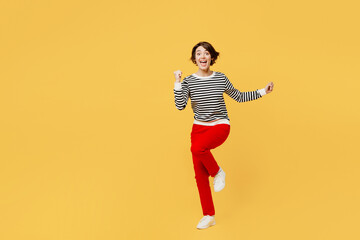 Full body young woman wear casual black and white shirt doing winner gesture celebrate clenching fists say yes raise up leg isolated on plain yellow color background studio portrait Lifestyle concept