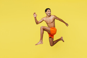 Fototapeta na wymiar Full body young sexy sporty man wear orange shorts swimsuit relax near hotel pool jump high look aside on area run fast isolated on plain yellow background. Summer vacation sea rest sun tan concept.