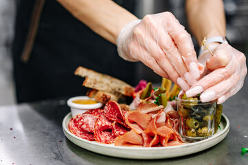 woman chef cooking Antipasto plate with ham, prosciutto, salami, cheese, vegetables and olives on kitchen