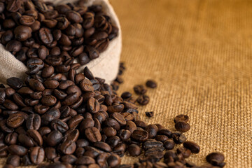 Heaps of roasted coffee beans in hemp bags and with seeds overflowing from the bag.