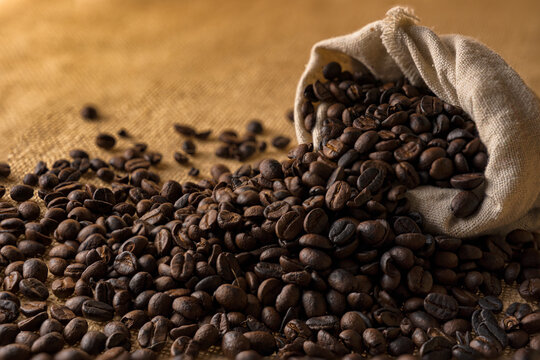 Heaps of roasted coffee beans in hemp bags and with seeds overflowing from the bag.