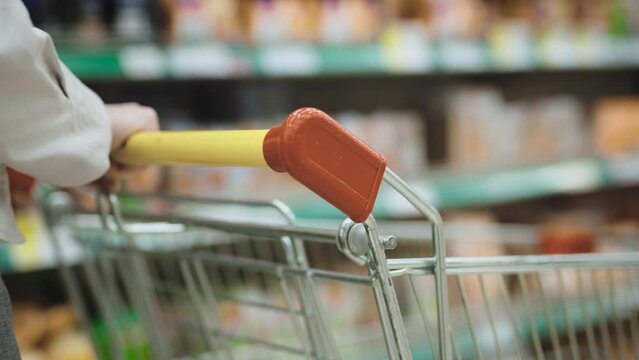 Unrecognizable woman in a supermarket with a cart. Close-up of hands pushing a grocery cart along the shelves