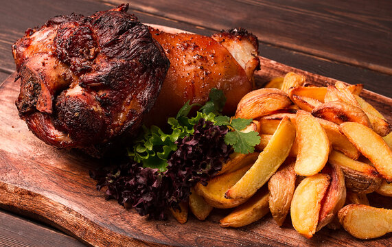 Pork knuckle, in soy-honey sauce, with fried potatoes, on a wooden chopping board, homemade, no people,