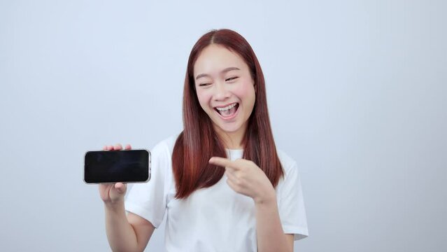 Smiling red-haired woman pointing at mobile phone isolated on white background with copy space.