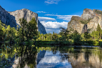 Panorama of the Yosemite Valley, including El Capitan, Cathedral Rocks and Bridalveil Falls, reflected at the Merced River in summer sunset.