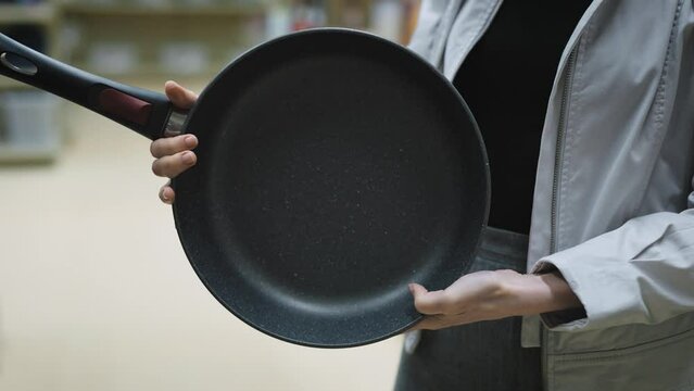Hands of woman holding a new pan, choosing black teflon frying pan, customer deciding to buy non-stick frying pan for cooking food in her kitchen