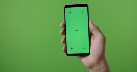 Hands of man holding a phone with vertical green chroma key screen. isolated on green background, swiping the touchscreen 