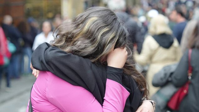 A long goodbye between two girls, embraced in the middle of a crowded city street