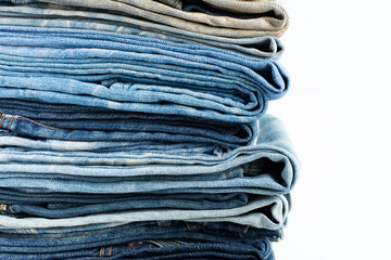 Stack of various shades blue jeans. Jeans stacked isolated on white background. Blue denim jeans texture banner with copy space for text design background. Canvas denim fashion texture