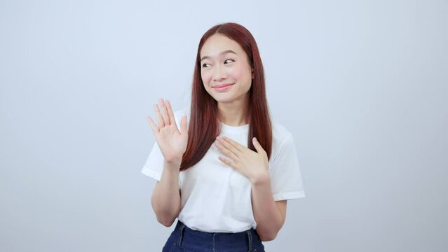 Cute young Asian student girl raises her hand and puts her palm on her chest.