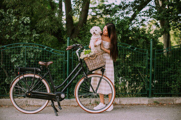 Fototapeta na wymiar Young woman putting white bichon frise dog in the basket of electric bike