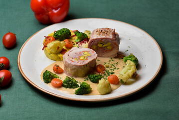Meat roll with broccoli, white cabbage, carrots, and mashed potatoes in a white plate on a dark green background.