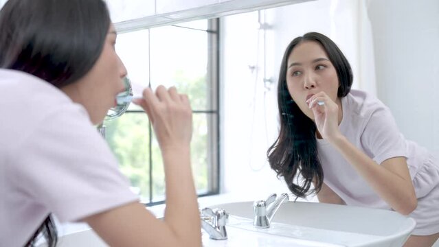 Happy Asian woman brushing her teeth in the bathroom in the morning.