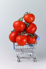 red juicy healthy fresh tomatoes only from the garden on a branch on a light background with a bottle of red ketchup and a grocery shopping cart