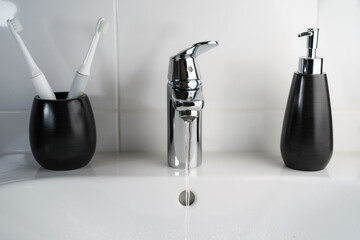 A jet of clean water flows from a faucet into a white sink. Selective focus.