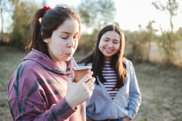 Two friends drinking yerba mate in the countryside at sunset. Copy space
