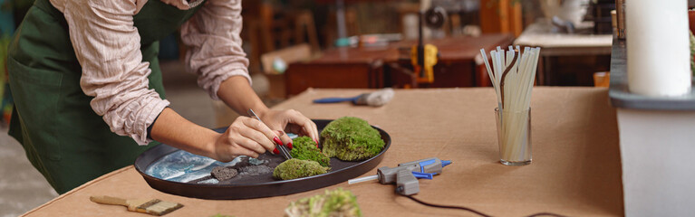 Focused woman decorator making green ikebana on tray with epoxy resin in florist workshop